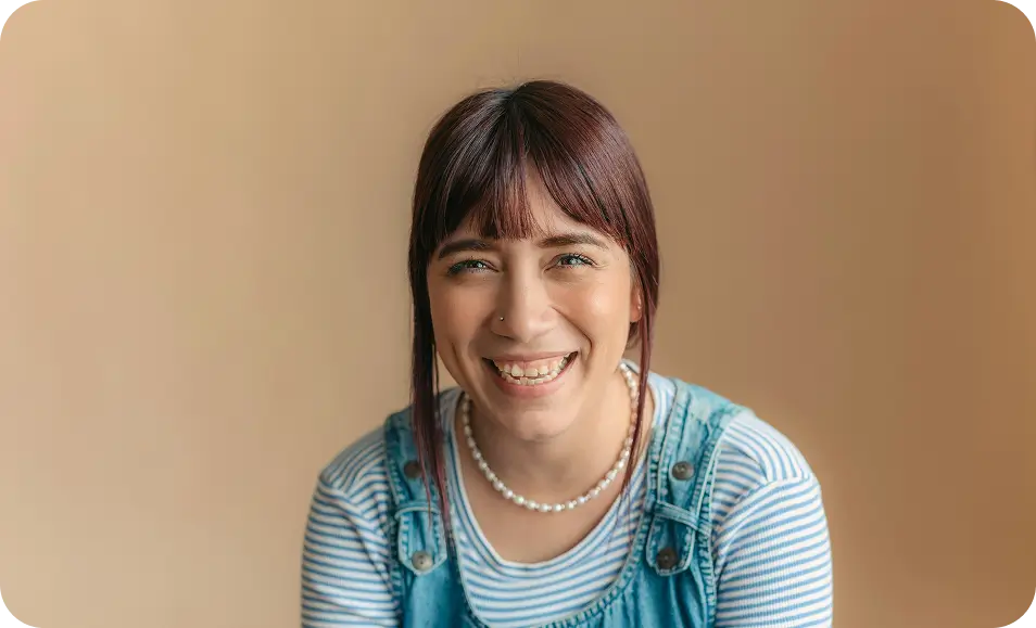 smiling woman in blue overalls and pearls sitting on a chair
