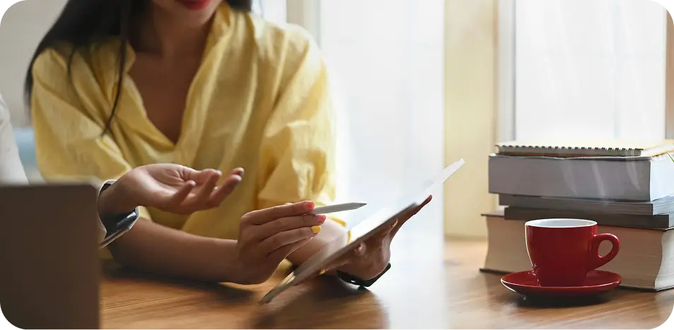 woman sitting at a table with a tablet and a cup of coffee