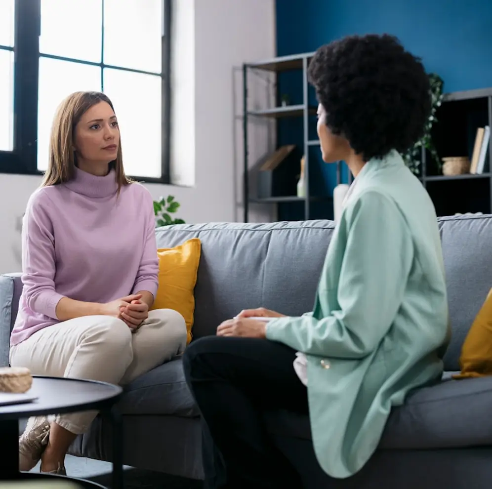 woman sitting on a couch talking to another woman in a living room