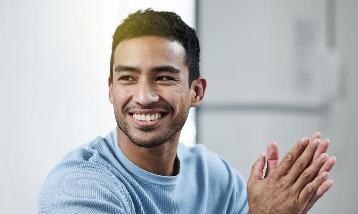 smiling man in blue sweater clapping with hands in front of him