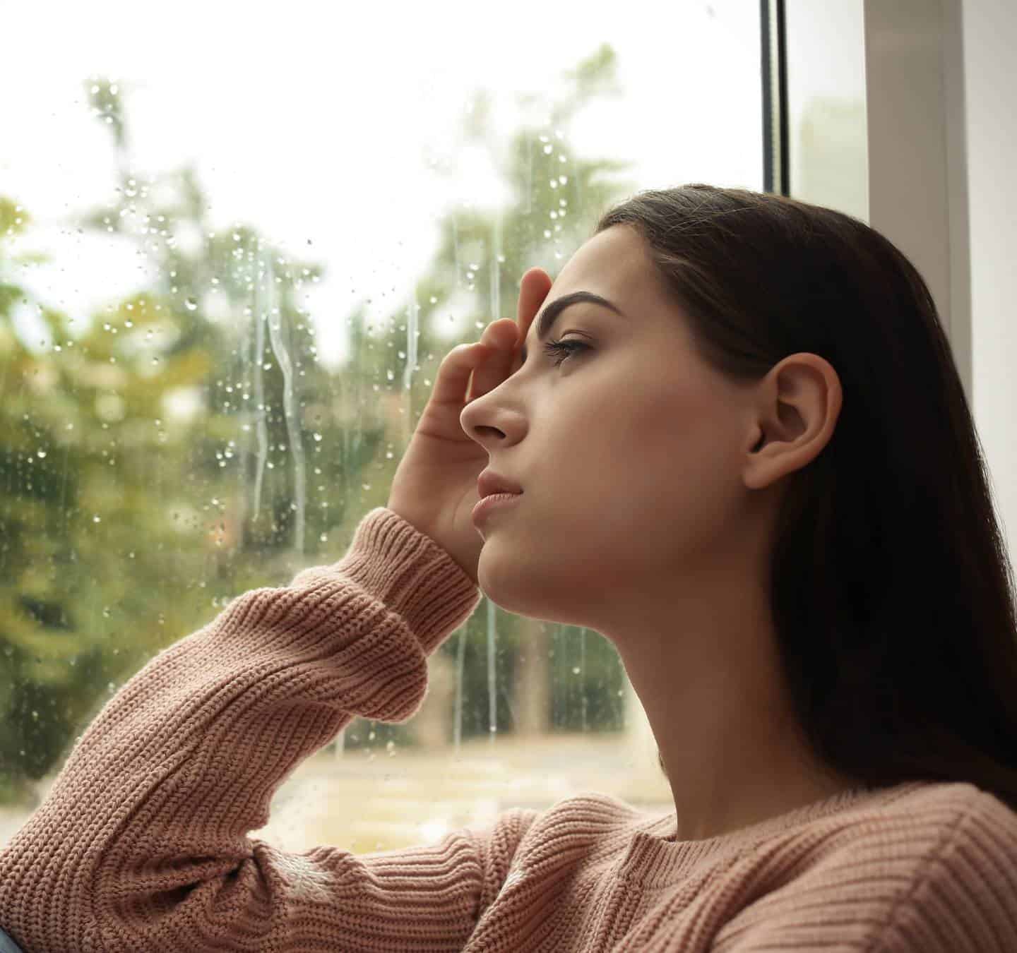 Woman quietly looking out a window while coping with depression and emotional struggles.