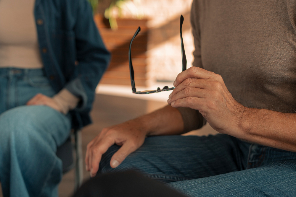 Man talking to a therapist while holding his glasses.