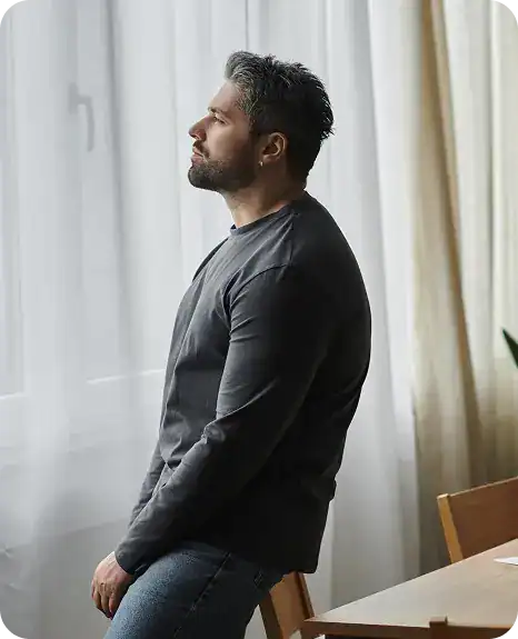 Man leaning on a chair in quiet reflection during his opioid use disorder treatment journey in MA at Rebuilding Recovery Center.
