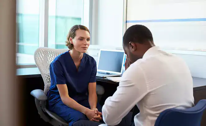A female doctor sitting in a chair, talking to a man in a white shirt about Substance Abuse Treatment Programs in Massachusetts