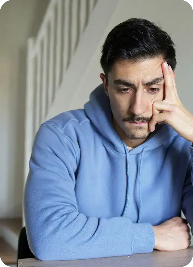 arafed man sitting at a table with his hand on his face thinking about Addiction Treatment in Bridgewater MA