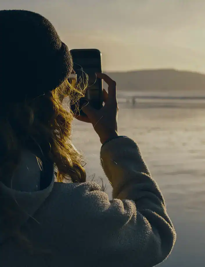 Woman taking a photo of the ocean while embracing a healthier future after fentanyl addiction treatment in Massachusetts at Rebuilding Recovery Center.