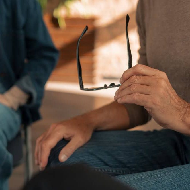 Man speaking with a therapist while holding his glasses during a dual diagnosis treatment session in Easton, MA at Rebuilding Recovery Center.